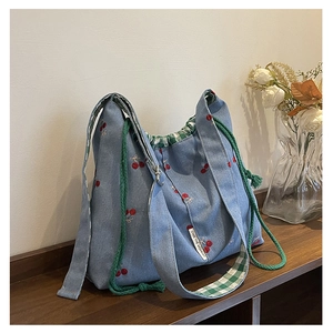 Detail of blue denim tote bag featuring red cherry embroidery and green drawstring closure