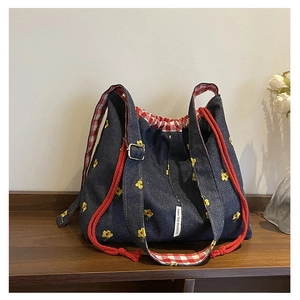 Detail of blue denim bucket bag with yellow floral embroidery and red drawstring cord