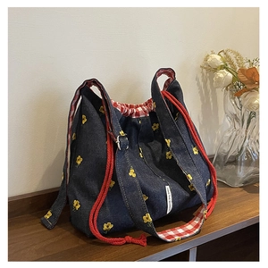 Detail of embroidered floral denim bucket bag with red rope drawstring and brand label