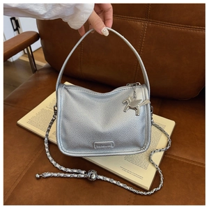 Detail of silver pebble leather handbag with chain strap and Pegasus charm on sofa