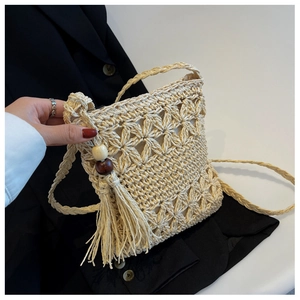 Détail du sac à téléphone en paille beige avec pompons et perles en bois décoratives