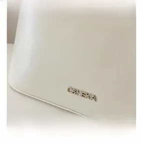 Close-up of silver metal logo and premium leather texture on white crossbody bag