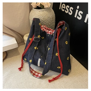 Detail of denim bucket bag featuring floral embroidery and red woven drawstring