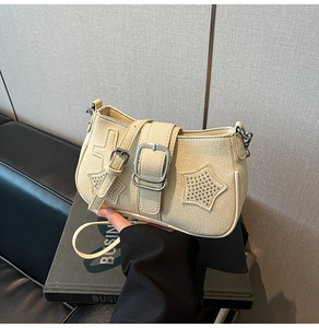 Detail of cream shoulder bag featuring star stud embellishments and silver buckle
