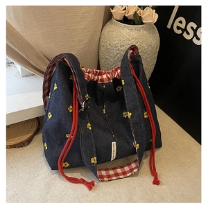 Detail of denim bucket bag with yellow floral embroidery and red checkered lining