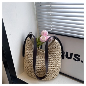Détail du sac seau en paille tressée avec bandoulière en cuir brun et tulipes roses