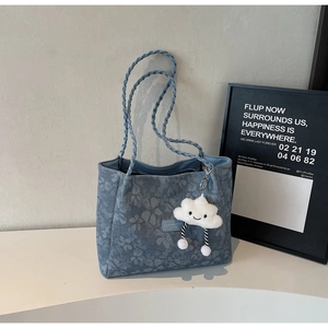Close-up of blue floral denim tote bag with woven handle and plush cloud pendant