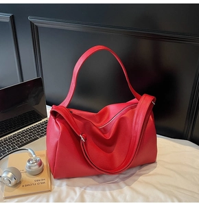 Close-up of red pebbled leather pillow bag with wide shoulder strap and metal zipper