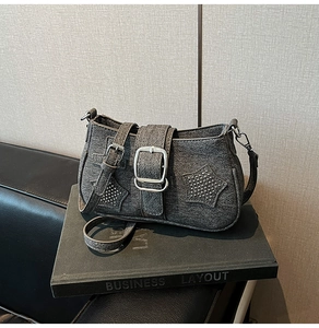 Macro detail of dark grey denim shoulder bag with silver star rivets and large metal buckle