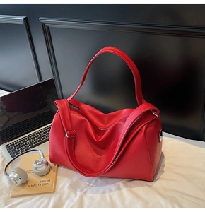 Detail view of large red leather Boston bag with laptop and headphones for commuting