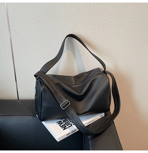 Detail of a black lychee texture Boston bag placed on a leather sofa with a book