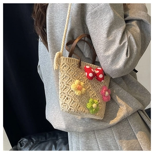 Detail of beige straw woven bucket bag with crochet flowers and red polka dot bow decoration