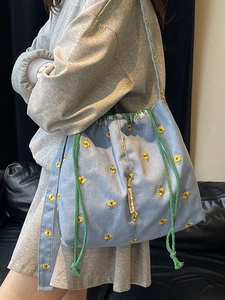 Light blue canvas shoulder bag with yellow flower embroidery and green drawstring closure
