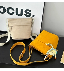Dettaglio di borse tote in nylon beige e giallo con logo ricamato e ciondolo carino