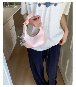 Detail view of pink pleated crescent handbag featuring silver bead charm and gathered handle