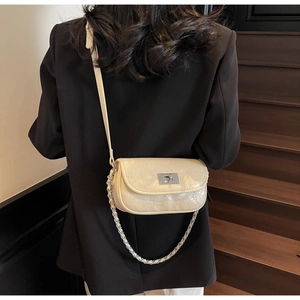 Detail of cream crossbody bag with silver lock on model wearing black blazer