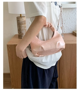 Detail of light pink cloud bag with pleated handle and metallic chain on a model