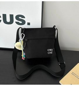 Dettaglio della borsa a tracolla in nylon nero con stampa OMQ CNH e ciondolo smiley