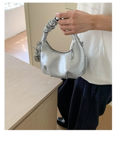 Detail of silver metallic pleated cloud bag with stylish chain and spherical charm