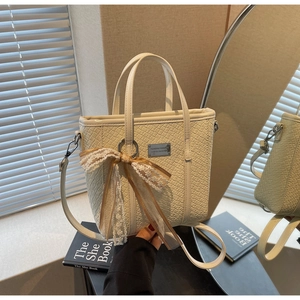 Dettaglio borsa tote intrecciata beige con nappa a fiocco in pizzo e placca metallica