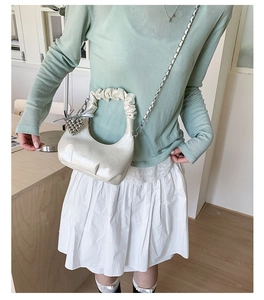 Detail of cream pleated cloud bag with silver chain handle and heart charm