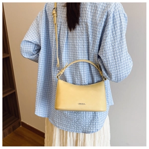 Detail of adjustable straps and brand logo on a soft yellow crescent shoulder bag