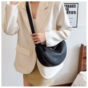 Detailed close-up of a black textured PU leather crescent bag worn with a white blazer