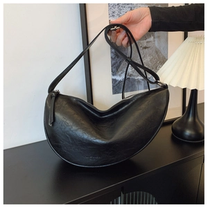Detail of black crescent bag featuring leather texture and silver zipper on a desk