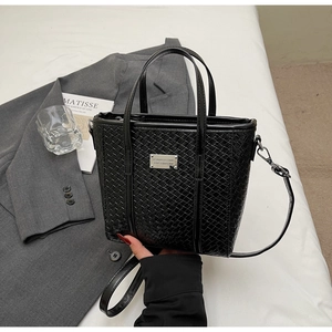 Dettaglio borsa nera intrecciata con placca d'argento su sfondo blazer grigio