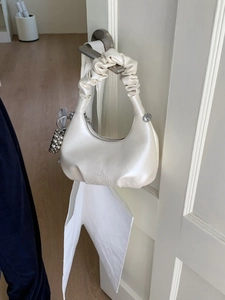 Chic cream ruched cloud bag with chain strap and beaded charm hanging on a door