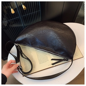 Detail showing the retro cracked leather texture and silver zipper of the crescent bag