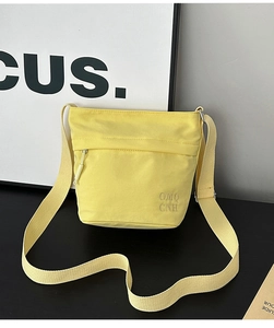 Dettaglio macro della borsa a tracolla in nylon giallo con ricamo di lettere e tasca frontale