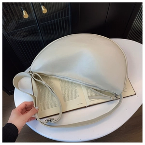 Detail of minimalist cream half-moon crossbody bag resting on an open book