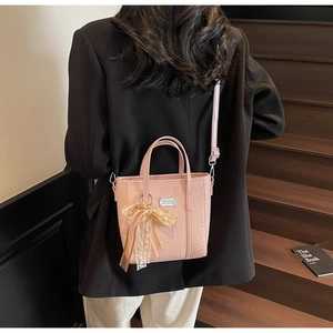 Dettaglio della borsa tote rosa intrecciata con ciondolo a fiocco e targhetta in metallo
