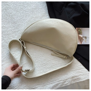 Detail of cream crescent crossbody bag with textured leather and silver zipper on white fabric