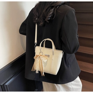 Dettaglio della borsa intrecciata beige con ciondolo a fiocco in pizzo e tracolla fine