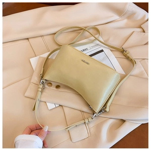 Close-up of cream leather shoulder bag with silver logo on beige blazer backdrop