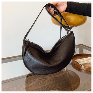 Detail of a coffee brown leather crescent bag with adjustable strap and embossed logo