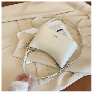 Detail of a creamy beige crescent shoulder bag with metal logo and adjustable strap
