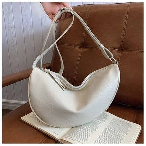 Detail of cream crescent bag with PU leather texture on a brown sofa with an open book