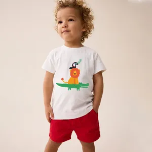 Dettaglio del set estivo per bambini con t-shirt bianca e stampa di leone e dinosauro