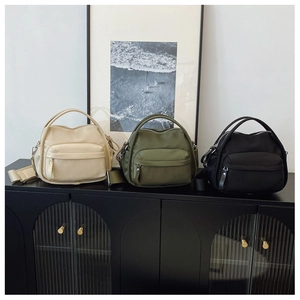 Three nylon crossbody bags in beige, olive and black lined up on a black modern cabinet