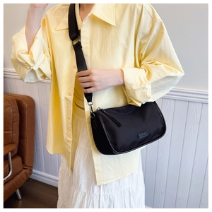 Sac cylindre noir à bandoulière large en toile porté par un mannequin élégant