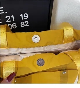 Detail view of yellow nylon tote bag featuring silver magnetic snap and smooth zipper closure