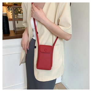 Detail of red textured leather mini crossbody bag worn by a model in a modern café setting