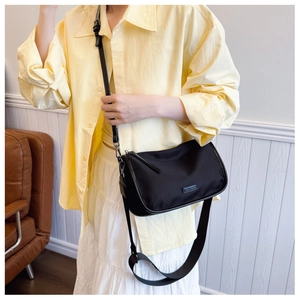 Détail d'un sac bandoulière en toile noire avec large sangle et logo métallique