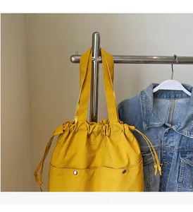 Detail view of a yellow waterproof nylon tote bag featuring drawstring closure and front pockets