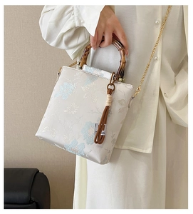 Detail of bamboo handle and blue floral embroidery on vintage style cream crossbody bag