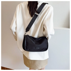Détail du sac bandoulière noir avec une large sangle et une plaque logo en métal