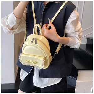 Detail eines cremegelben Mini-Rucksacks mit eleganter Spitze und einer großen Schleife